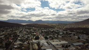 Sıralanmış sokakların ve yeşil alanların arka planda dağların olduğu bir şehir manzarası