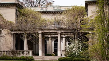 Bitkilerle çevrili büyük sütunları olan bir Viktorya dönemi binası.