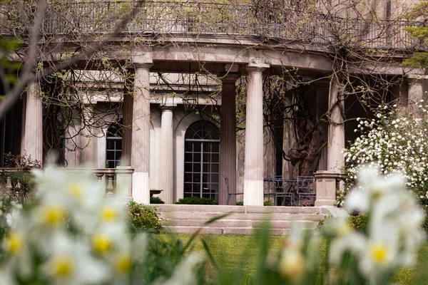 Bitkilerle çevrili büyük sütunları olan bir Viktorya dönemi binası.