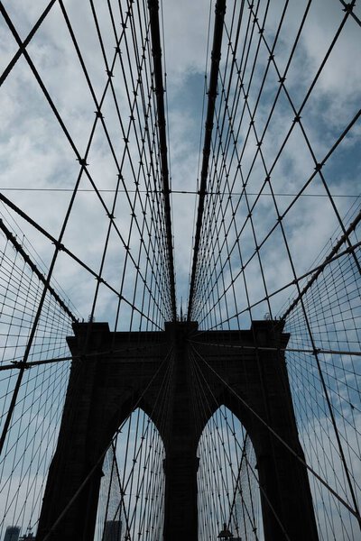 A vertical low angle shot of the top cables of Brooklyn Bridge against blue cloudy sky