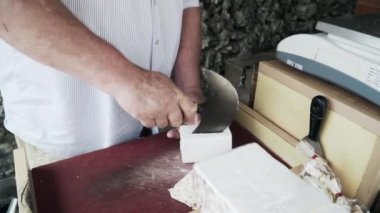 Tahta bir masada özel bir bıçakla peynir kesen bir adamın görüntüsü.