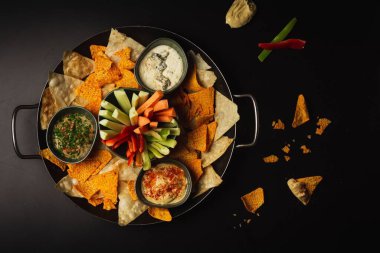 Aperatif kasesinin en iyi pozu. Siyah bir masada doğranmış sebze cipsi ve çorba.