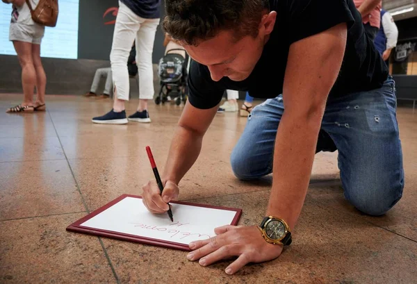 Young Hispanic Man Sitting Floor Writing Airport Welcome Greeting — Stock Photo, Image