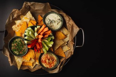 Aperatif kasesinin en iyi pozu. Siyah bir masada doğranmış sebze cipsi ve çorba.