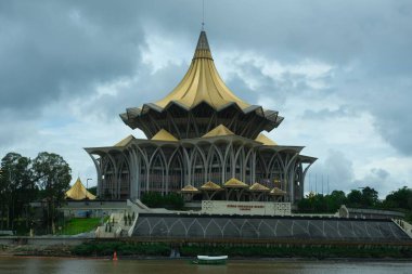Dewan Undangan Negeri or Sarawak Devlet Meclisi 'nin yanından geçen bir tekne ve bulut görüşlü bir resmi..