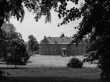 Ağaçların çerçevesinden eski bir malikanenin gri renkli bir görüntüsü.