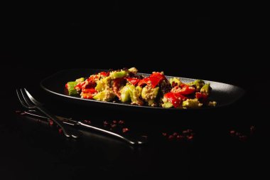 Siyah bir masada servis edilen kırmızı biber ve sebze salatası.