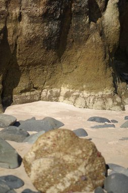 Kayalık uçurumun kenarındaki kumlu sahilde büyük mavi çakıl taşlarının dikey görüntüsü.