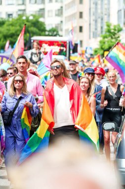 İsveç Malmö Gururu 'nda omuzlarında gurur bayrağı taşıyan bir grup insanla sokakta yürüyen yakışıklı bir adam.