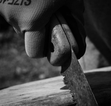 Testereyle odun kesen eldivenli bir elin gri tonda yakın çekimi.