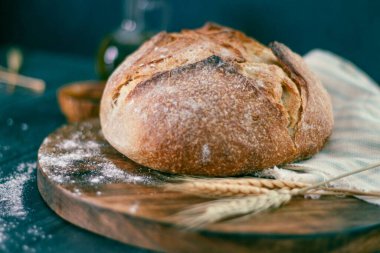 Tahta bir yüzey üzerinde buğday bitkileriyle ekşi ekmeğin yakın plan çekimi.