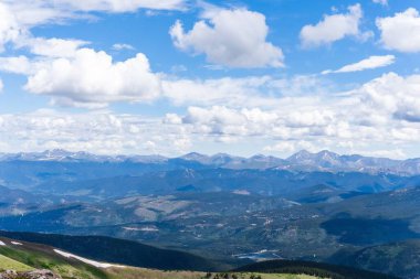 Gökyüzünün altındaki tepeleri ve dağları kabarık bulutları olan güzel bir vadi manzarası.