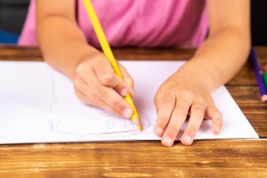 Tahta masaya resim çizen bir çocuğun elleri.