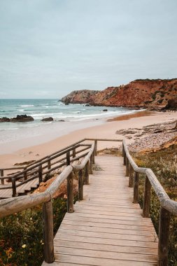 Praia do Amado 'nun güzel plajı Algarve' ın batısında bulutlu bir günde. Dalgalı okyanusu sörfçü grupları dolduruyor.
