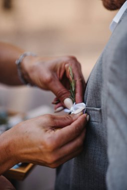 Damadın annesinin, damadın takım elbisesine çelenk taktığı dikey bir fotoğraf.