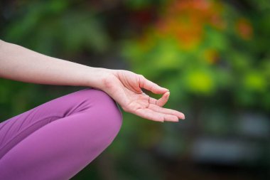 Kafkasyalı kadın yogini 'nin dizinde bir el, yeşil bulanık arka plan üzerinde meditasyon yapıyor.
