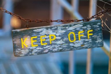 Bulanık bir arkaplanda paslı metal bir zincire tutturulmuş ahşap plakaya 