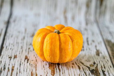 Beyaz ahşap yüzeyde küçük turuncu balkabağı yakın plan.