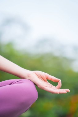 Kafkasyalı kadın yogini 'nin dizinde bir el, yeşil bulanık arka plan üzerinde meditasyon yapıyor.