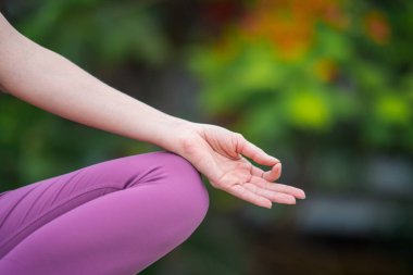 Kafkasyalı kadın yogini 'nin dizinde bir el, yeşil bulanık arka plan üzerinde meditasyon yapıyor.