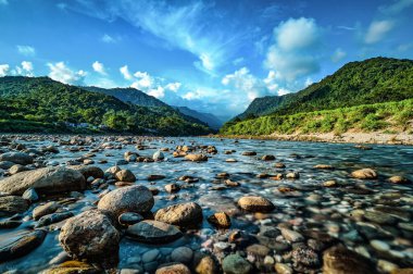 Şeffaf, sığ sularda, arka planda orman dağları olan güzel bir kaya görüntüsü.