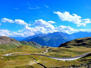 Mavi arkaplanı olan yeşil bir dağda virajlı bir yol