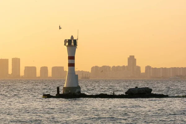日落时以城市为背景的水平海景 中间有座灯塔 — 图库照片