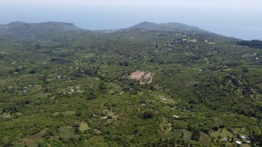 Arka planda deniz olan yeşil kaplı bir dağın havadan görünüşü.