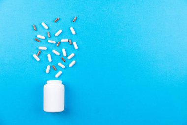 Mavi arka planda şişeden bir avuç dolusu hap döküldü.