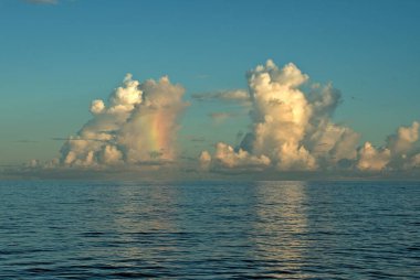 Mavi deniz suyunun üzerindeki tüylü beyaz bulutların doğal manzarası.