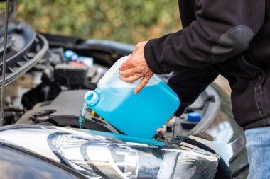 Arabanın ön cam sileceği suyunu dolduran bir adamın yakın plan fotoğrafı.