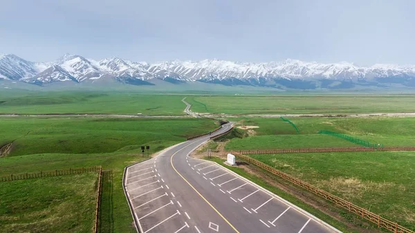 Uma Estrada Asfalto Construída Campo Verde Com Montanhas Cobertas Neve — Fotografia de Stock