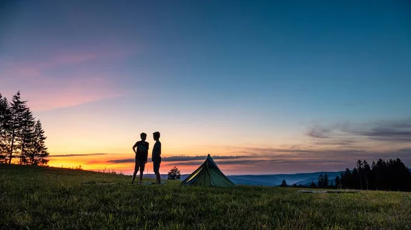 丘の上のテントのそばに二人の男の子が立っていたシルエットで 背景には夕日が入っていた — ストック写真