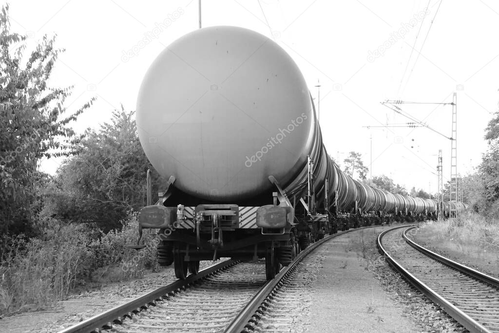 The grayscale view of the cargo train with oil tanker cars