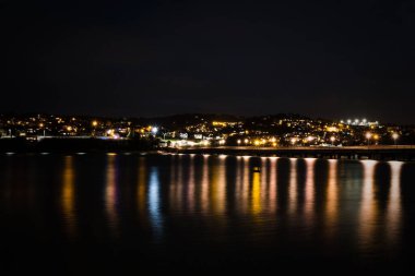Güzel bir çekim Aydınlatılmış bir şehir ve suda yansıyan ışıklar