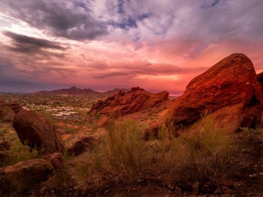 Güneşin batışında pembe-turuncu bulutlu bir gökyüzünün verimsiz, kayalık bir arazide nefes kesen görüntüsü.