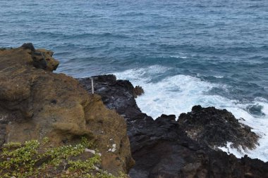 Bulutlu bir günde okyanus dalgalarının kayalık bir plaja çarpmasının manzarası.