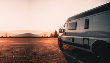 Yolun kenarına park etmiş bir karavan manzaralı bir günbatımına karşı.