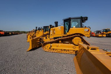 Açık mavi gökyüzünün altında raylı pedleri olan bir sıra buldozer.