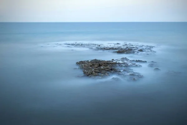 霧が水を覆っている岩の多い海の美しいショット 背景のために素晴らしい — ストック写真