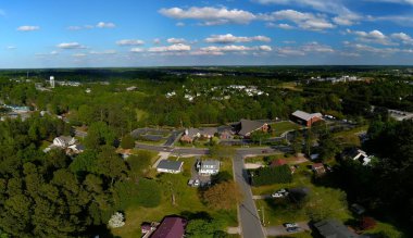 Arka planda mavi gökyüzü olan bir ormanın yakınındaki banliyö mahallesinin insansız hava aracı görüntüsü.