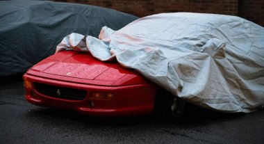Yağmurda kırmızı bir Ferrari kısmen araba kılıfıyla kaplı.