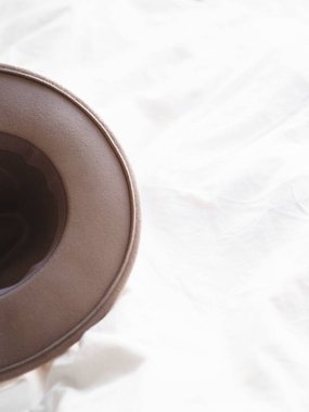 Beyaz çarşafların üzerinde şık bir şapkanın dikey çekimi.