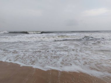 Deniz köpüğü ve dalgaları gri gökyüzünün altında Calangute sahilinde