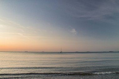 Gün batımında ortasında yüzen bir tekneyle sakin bir deniz manzarası.