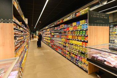 Bir sıra dolu süpermarket rafları ve ortasında duran bir insan.