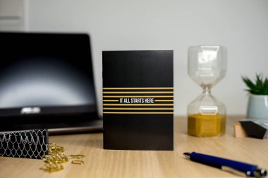 Motivasyon planlayıcısı, dizüstü bilgisayarı, kum saati ve kırtasiyesi olan tahta bir ofis masası.