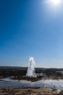 Açık mavi gökyüzüne karşı bir Geysir dikey görüntüsü.