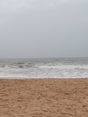 Gri gökyüzünün altında, Calangute sahilindeki denizin dikey görüntüsü.