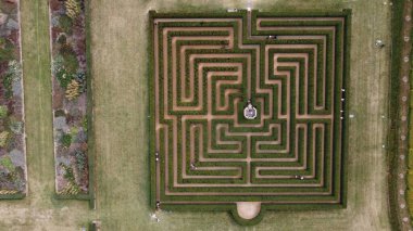 Bahçesinde çiçek şeritleri olan kare bir labirentin havadan çekilmiş bir fotoğrafı.